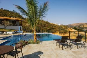 a pool with chairs and a palm tree next to a house at Pousada Enseada da Ilha in Capitólio