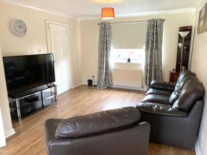uma sala de estar com um sofá de couro e uma televisão em Dada Apartment em Glasgow