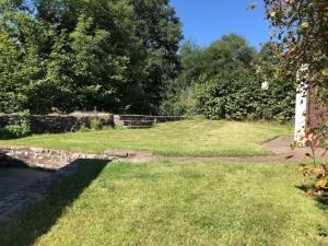 a grassy yard with a stone wall and trees at Cobblers Cottage in Brecon Beacons in Brecon