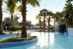 ein Swimmingpool mit Palmen in einem Ferienresort in der Unterkunft Montrose - A Mayfair Collection Hotel in Kuwait