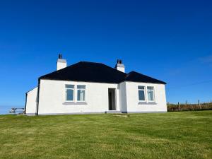 a white house with a black roof on a grass field at Dun Buidhe in Pollachar
