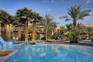 a swimming pool with palm trees in front of a resort at Mövenpick Hotel Kuwait in Kuwait