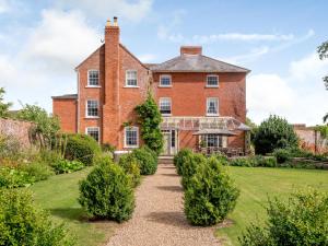 una vieja casa de ladrillo con arbustos delante de ella en Hilltop House en Tenbury