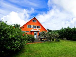 an orange house on a grassy field with trees at 陽のあたる宿 サンセットパーム in Oshima