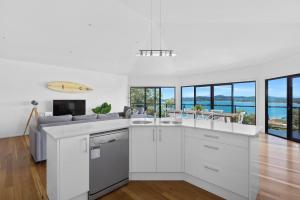 a kitchen with white appliances and a living room with windows at Wanda Point House - pure tranquillity and walk to beach in Salamander Bay