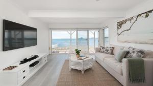 a white living room with a couch and a tv at The Beach Shack on Wanda - Waterfront Coastal Chic in Salamander Bay