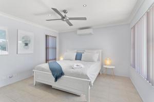 a white bedroom with a bed and a ceiling fan at Above and Beyond - Beautiful Home with Heated Pool and Views in Salamander Bay