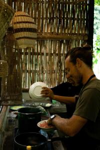 Bali Jungle Camping by Amerta Experience في تابانان: رجل يعد طبق من الطعام في مطبخ