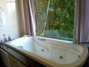 La salle de bains est pourvue d'une baignoire blanche et d'une fenêtre. dans l'établissement Chalé Recanto do Sol, à Paraisópolis