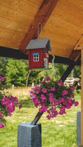 Ein Vogelhaus hängt von einer Veranda mit lila Blumen. in der Unterkunft Acasă Straja - Casa Nordică in Lupeni