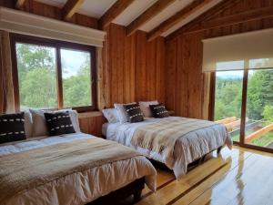 two beds in a room with wooden walls and windows at PARCELA DE AGRADO CON PISCINA LAGO RANCO todas las instalaciones con uso exclusivo capacidad 20 personas in Lago Ranco