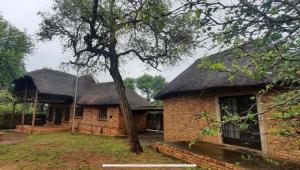 a brick building with a thatched roof and a tree at Intundla's Rest in Marloth Park