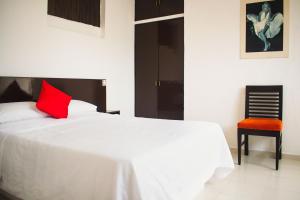 a white bed with a red pillow and a chair at Hotel Cupules in Mérida