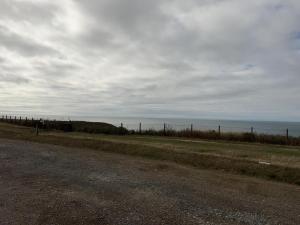 a dirt road next to the ocean with a fence at Sea Facing 2BD Terraced Home - Peacehaven in Peacehaven