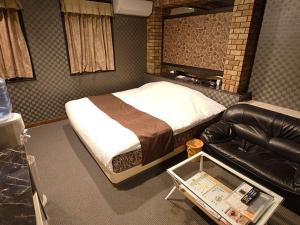 a bedroom with a bed and a leather couch at フラミンゴ　大人専用 in Yoshioka