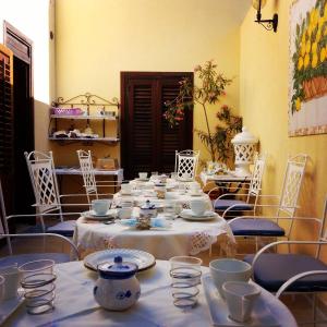 un lungo tavolo con tavoli e sedie bianchi con ciotole e tazze di AFFITTACAMERE A TRE MINUTI IN SPIAGGIA Il Veliero a San Vito lo Capo