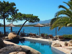 a swimming pool with chairs and umbrellas next to the water at Maranatha, front de mer avec plage in Porto-Vecchio