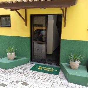 Apartamentos e Flats Praia das Toninhas - Ubatuba في أوباتوبا: مبنى أخضر وأصفر مع وجود اثنين من النباتات الفخارية في الأمام