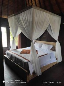 een slaapkamer met een hemelbed en witte gordijnen bij TEGESWOODHOUSE A with WiFi,Ac in Ubud