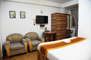 um quarto de hotel com duas cadeiras e uma cama e uma televisão em PHIBHA VILLA em Shillong