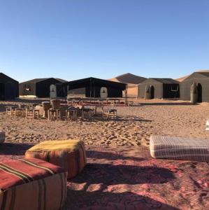 Chegaga desert Trips camp في امحاميد: مجموعة من الخيام في الصحراء مع طاولات وكراسي