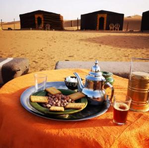 Chegaga desert Trips camp في امحاميد: طبق من الطعام على طاولة مع إبريق الشاي والوجبات الخفيفة