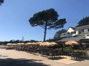 een groep tafels en stoelen met parasols en een boom bij Petite maison avec piscine à 500m de la plage in Guidel