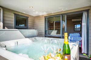 The Grand @ Taupo في تاوبو: حوض استحمام ساخن مع كأسين وزجاجة من النبيذ