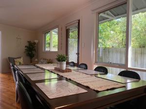 uma mesa longa com cadeiras num quarto com janelas em Invy Escape em Inverloch