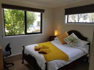 a bedroom with a bed with yellow sheets and two windows at Torquay Homestay Guesthouse in Torquay