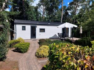 a small white cabin with a table and an umbrella at Heerlijk chalet in prachtige natuur. in Doornspijk