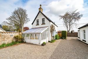 una casa blanca con un invernadero en la entrada en Robins Nest Cottage, en Blairgowrie