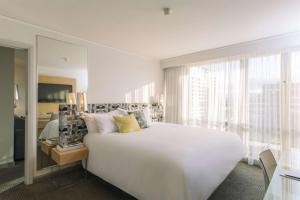 a white bedroom with a large bed and a window at QT Canberra in Canberra
