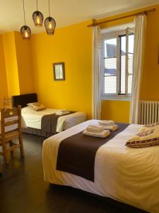 two beds in a room with yellow walls and a window at Hôtel du Château in Annecy