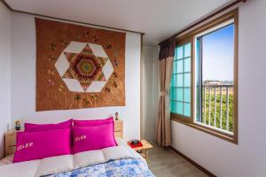 um quarto com uma cama com almofadas cor-de-rosa e uma janela em Jeju Wayo Pension em Jeju