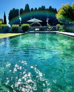 una piscina de agua azul con un arco iris en el fondo en Le Pavillon de Galon, en Cucuron