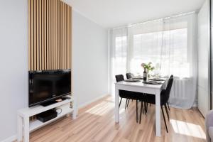 a white dining room with a table and a tv at Seaview Apartment Gdańsk Przymorze by Renters in Gdańsk