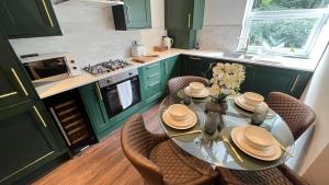 una cocina con armarios verdes y una mesa de cristal con sillas. en Park View, en Headingley