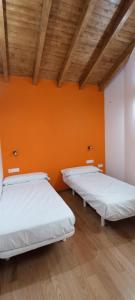 two beds in a room with an orange wall at Alojamientos playa del silencio in Castañeras