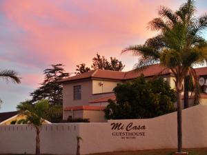 a house in front of a fence with palm trees at Mi Casa Guest House in Uitenhage