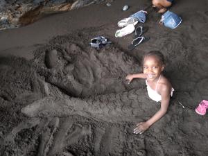 een klein meisje liggend in het zand op het strand bij Black Mamba in Paul