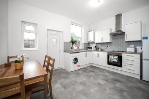 uma cozinha com armários brancos, uma mesa e um fogão em Modern spacious 2 bedroom house in Leigh Self Service em Leigh