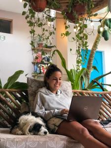 a woman sitting on a couch with a laptop and a dog at Barco Verde Hostel in Holbox Island