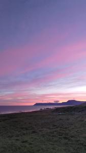 a field with a sunset in the sky over the ocean at Rau&eth;sdalur in Brj&aacute;nsl&aelig;kur