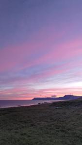 un campo con una puesta de sol en el cielo sobre el océano en Rauðsdalur, en Brjánslækur