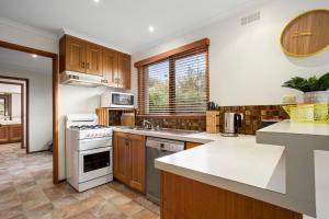 una cocina con armarios de madera y electrodomésticos blancos en Lonnie Pad, en Point Lonsdale