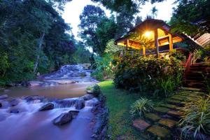 a house next to a river next to a forest at Sukantara Cascade Resort and Spa in Mae Rim