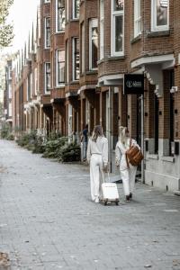 twee vrouwen die over straat lopen en een koffer trekken bij Le Petit Marin Boutique Hotel in Rotterdam