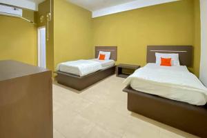 two beds in a room with yellow walls and orange pillows at KoolKost Syariah near Stasiun Tanjung Karang Lampung in Bandar Lampung