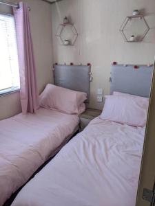 2 Betten in einem kleinen Zimmer mit rosa Vorhängen in der Unterkunft Immaculate Sen friendly 3-Bed caravan in Porthcawl in Porthcawl